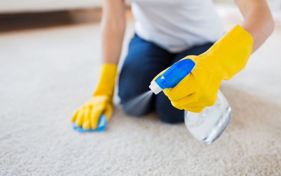 a person wearing yellow gloves spraying a spray on carpet