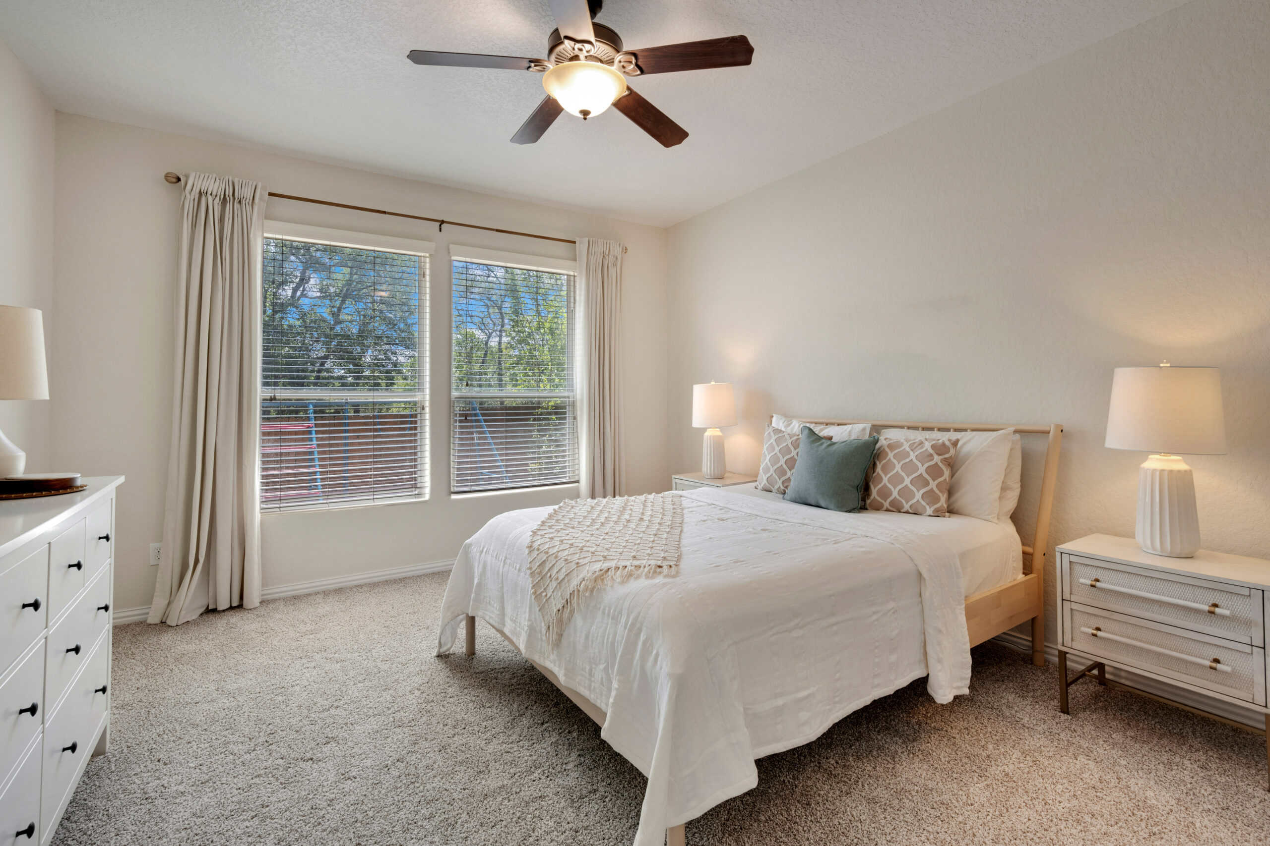 Bright and airy bedroom with large windows, ceiling fan, and comfortable bedding.