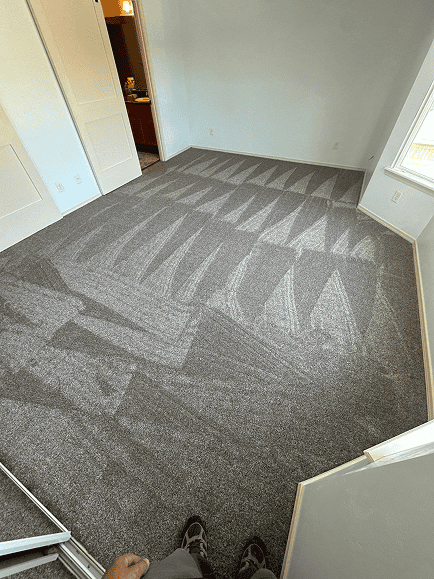 Newly installed gray carpet in a bright, clean room with sunlight and large windows.