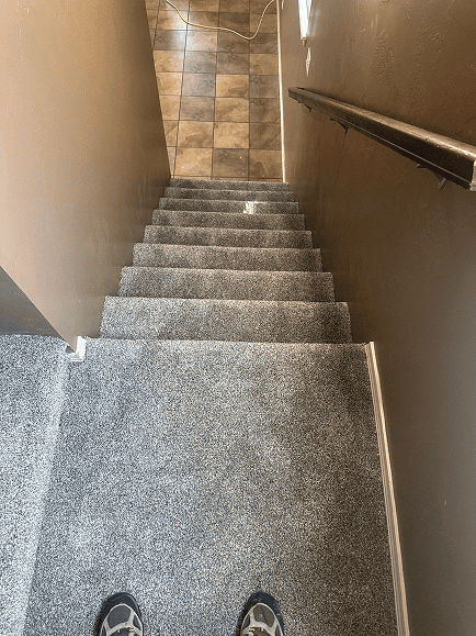 Staircase with new gray carpet flooring, leading to a tiled area at the bottom.
