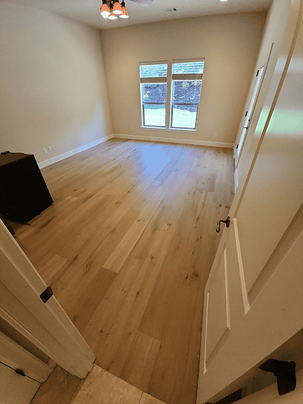 Beautiful new hardwood flooring in a bright, empty room with large windows.