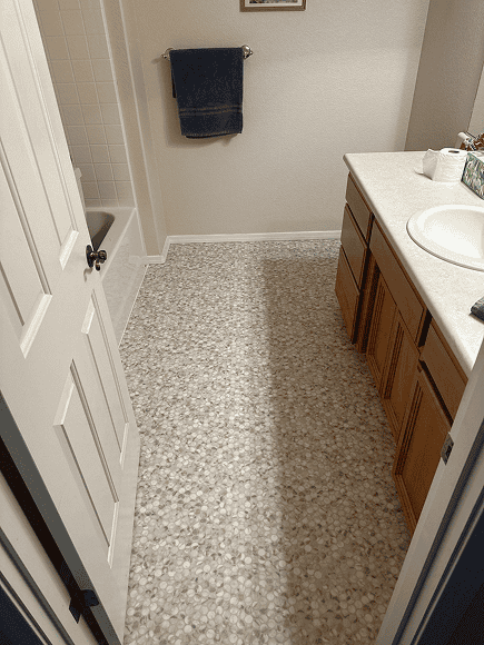 Beautifully installed pebble stone flooring in a bathroom with vanity and towel rack.