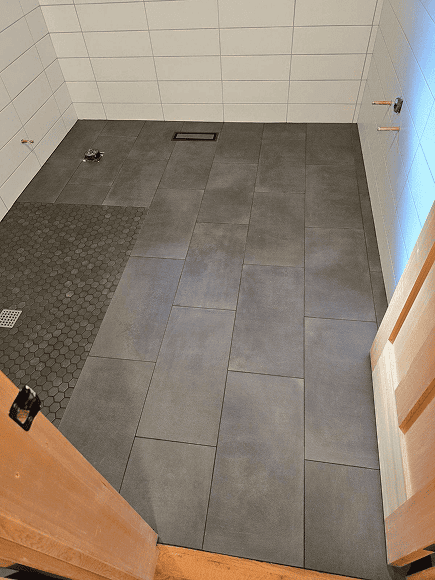 Bathroom tile installation with large gray tiles and a textured black section.