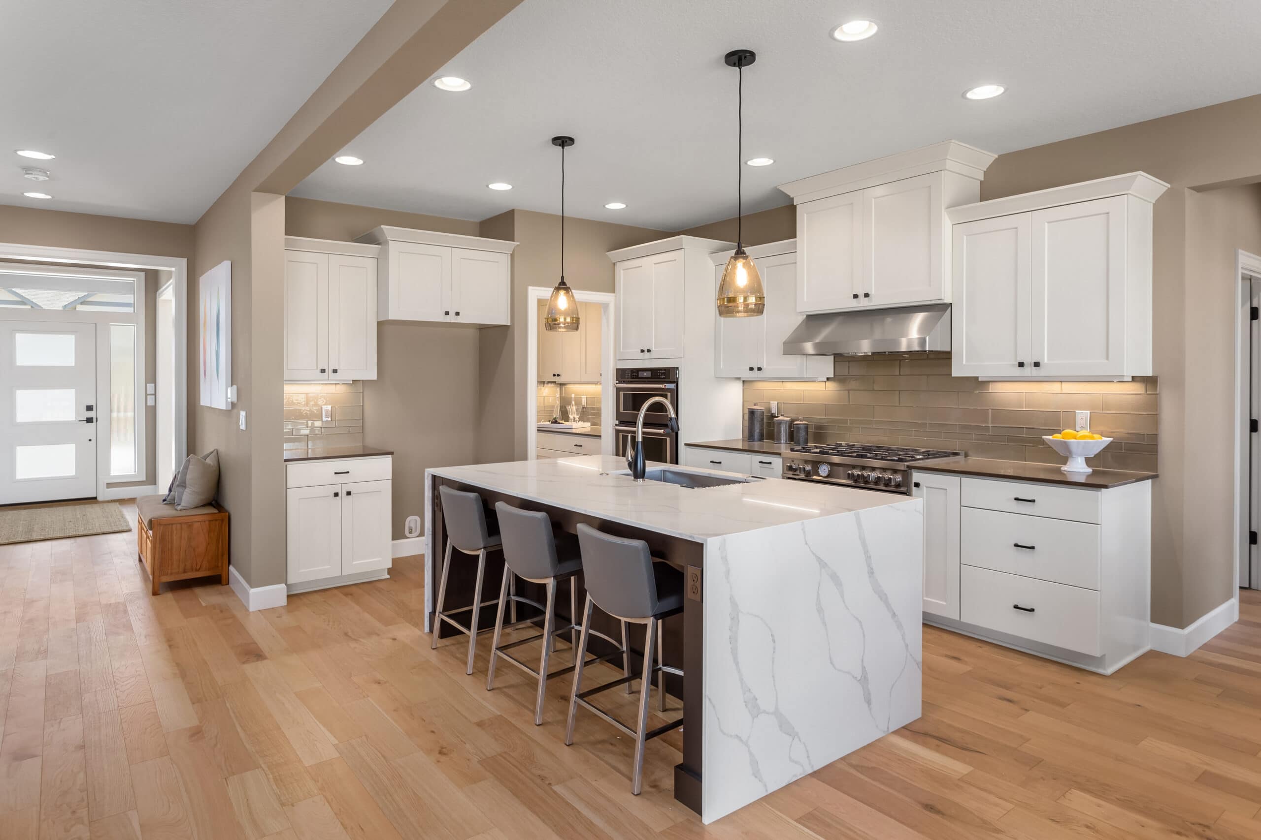Bright modern kitchen with white cabinets, marble island, and pendant lighting.